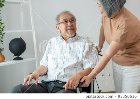 Senior wife giving support to her husband in his wheelchair with love. 95350610