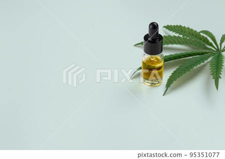 Legalized cannabis sativa hemp leaf and container of CBD oil with dropper lid. 95351077