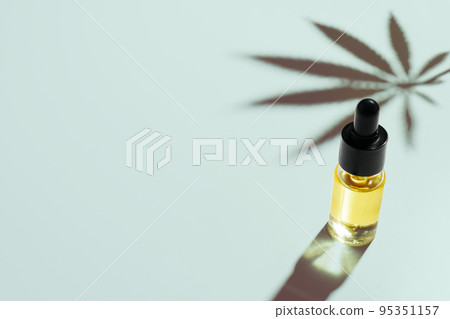 Legalized cannabis sativa hemp leaf and container of CBD oil with dropper lid. 95351157
