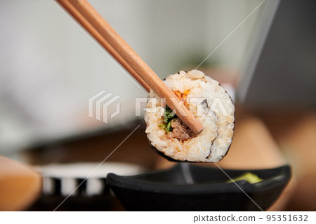 Closeup image of woman dipping sushi in small bowl of soy sauce Closeup image of woman dipping sushi in small bowl of soy sauce 95351632
