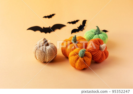 Knitted orange, green and beige pumpkins and black bats on an orange background, autumn composition, front view. Halloween concept. 95352247