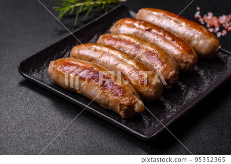 Tasty grilled sausages with spices and herbs on a black slate plate 95352365
