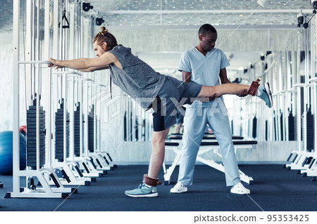 Patient exercising in gym with therapist 95353425