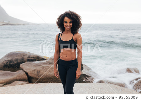 Smiling woman in fitness wear posing against the ocean after training	 95355009