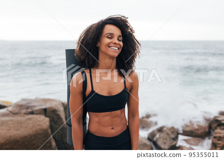 Laughing woman with closed eyes standing by the ocean after yoga training Laughing woman with closed eyes standing by the ocean after yoga training 95355011