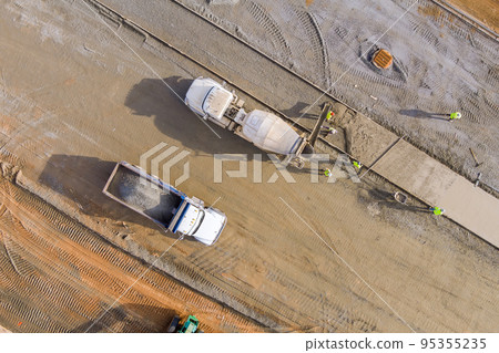 There is concrete mixer truck that pouring concrete mortar to sidewalk workers while construction is underway There is concrete mixer truck that pouring concrete mortar to sidewalk workers while construction is underway 95355235