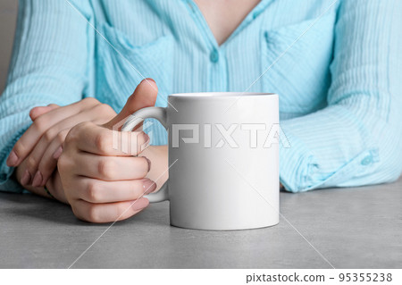Girl in blue shirt holding white porcelain coffee mug mock up on the grey stone table Girl in blue shirt holding white porcelain coffee mug mock up on the grey stone table 95355238