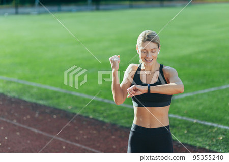 Satisfied with the result of training and running, the athlete looks at the smart watch, the blonde holds her hand up and celebrates the victory. Satisfied with the result of training and running, the athlete looks at the smart watch, the blonde holds her hand up and celebrates the victory. 95355240
