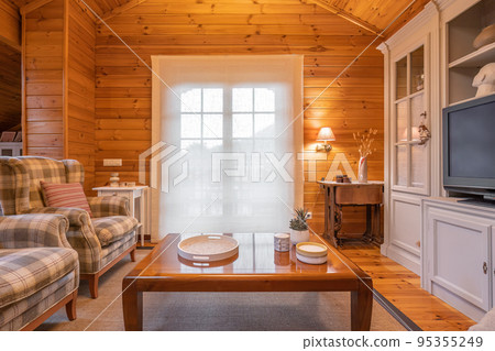 Cozy interior of a country house in a wooden design. Spacious living room with chairs, table and big cupboard 95355249