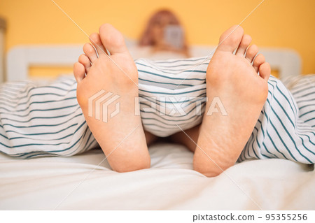Woman feet on the bed under white blanket. Sleeping and relax concept. Vacation and Holiday theme Woman feet on the bed under white blanket. Sleeping and relax concept. Vacation and Holiday theme 95355256