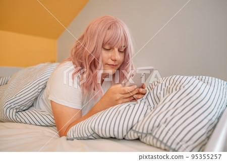 Relaxed woman at home reading a text message in her bright bedroom Relaxed woman at home reading a text message in her bright bedroom 95355257