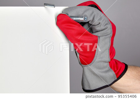 A hand in a red protective glove inserts a confirmation into a hole in a furniture shield. Assembly and repair of furniture 95355406