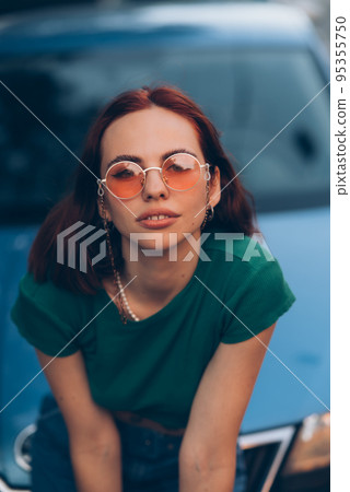 Beautiful girl sits on the hood of a blue car Beautiful girl sits on the hood of a blue car 95355750