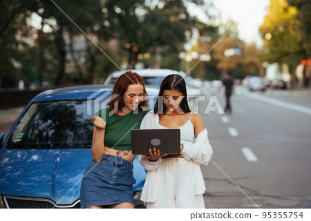 Two young women with a laptop near the car Two young women with a laptop near the car 95355754
