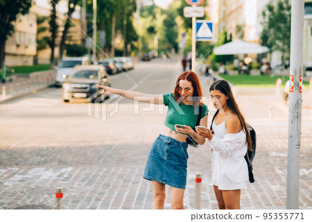 Two tourist friends consulting an online guide on a smart phone in the street 95355771