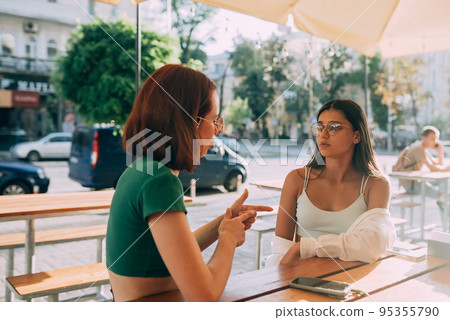 Two pretty girlfriends talking while sitting in a bar outdoors 95355790