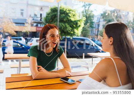 Two pretty girlfriends talking while sitting in a bar outdoors 95355800