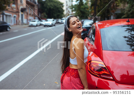 Portrait of pretty Caucasian woman standing against new red car 95356151