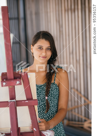 Young beautiful artist stands near an easel with a canvas 95356157