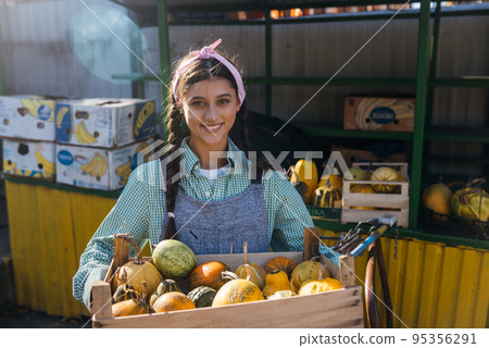 Farmer woman holds a wooden box with pumpkins in her hands Farmer woman holds a wooden box with pumpkins in her hands 95356291