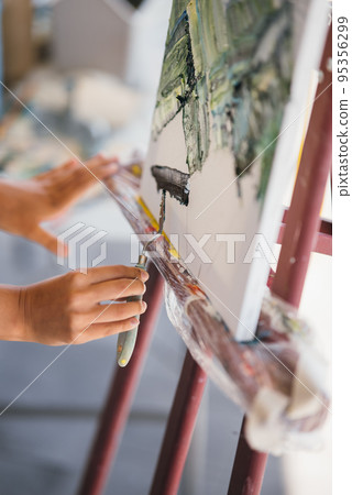 Close-up of a woman's hand applying paint to a canvas Close-up of a woman's hand applying paint to a canvas 95356299