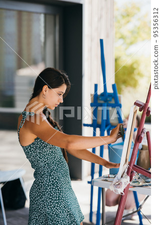 Young woman artist paints with a spatula on the canvas Young woman artist paints with a spatula on the canvas 95356312
