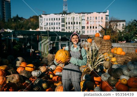 Happy farmer woman in a denim jumpsuit holds ripe pumpkin Happy farmer woman in a denim jumpsuit holds ripe pumpkin 95356439