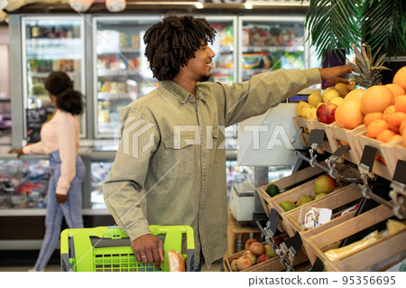 African Man Shopping Groceries Taking Fruits From Shelf In Supermarket African Man Shopping Groceries Taking Fruits From Shelf In Supermarket 95356695