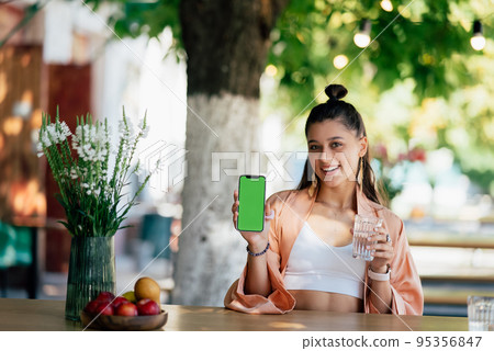 Young woman is holding a smartphone with a green screen 95356847