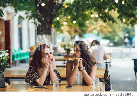 Two young beautiful women girlfriends talking in an outdoor cafe 95356943