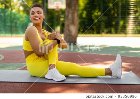 Smiling Black Sporty Woman In Yellow Sportswear Stretching Leg Outdoors Smiling Black Sporty Woman In Yellow Sportswear Stretching Leg Outdoors 95356986
