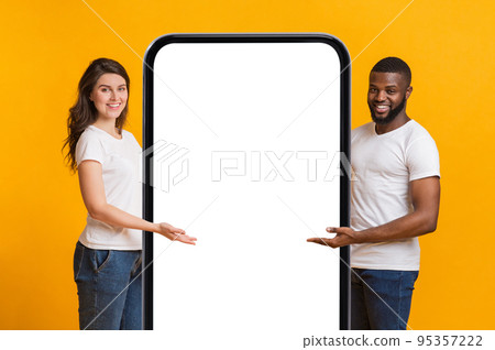 Happy Interracial Couple Pointing At Big Blank Smartphone With White Screen Happy Interracial Couple Pointing At Big Blank Smartphone With White Screen 95357222