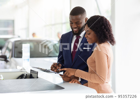 Black Woman Discussing Agreement Details With Manager While Buying Car In Showroom 95357226