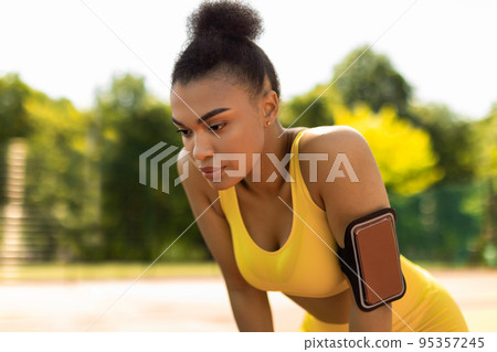 Sporty black woman in yellow sportswear resting breathing after run Sporty black woman in yellow sportswear resting breathing after run 95357245