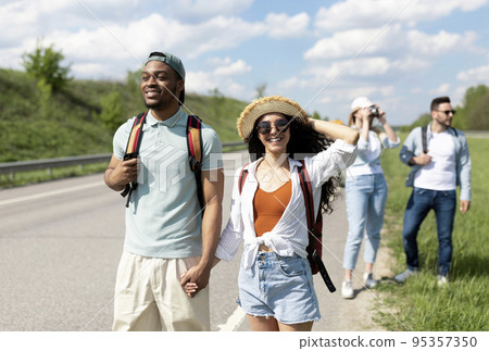 Young black guy and his girlfriend traveling together with multinational friends, hitchhiking during summer vacation Young black guy and his girlfriend traveling together with multinational friends, hitchhiking during summer vacation 95357350