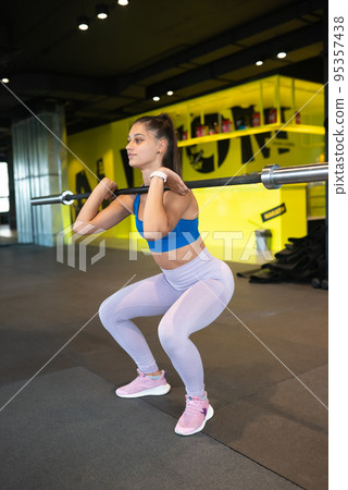 Strong young woman doing sit-ups with a barbell Strong young woman doing sit-ups with a barbell 95357438