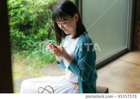 一個年輕女子在門廊上看智能手機 一個年輕女子在門廊上看智能手機 95357578