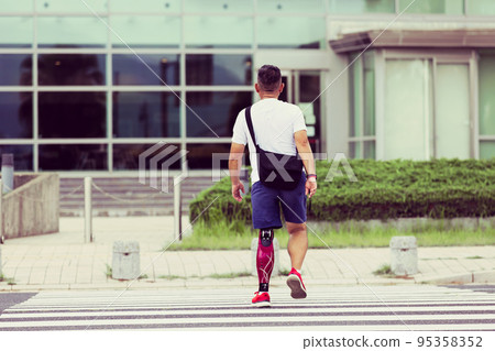Disabled man with a prosthetic leg crossing the pedestrian crossing 95358352