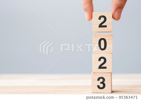 hand holding wooden cube block with 2023 text on table background. hand holding wooden cube block with 2023 text on table background. 95363471