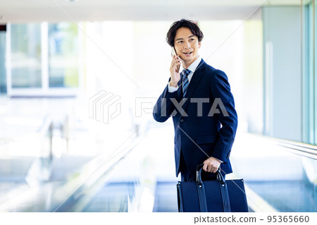 年輕商人在辦公室大堂打電話給智能手機 95365660