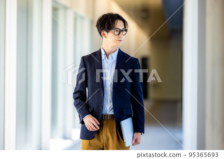 辦公室走廊裡帶智能手機的微笑年輕人 辦公室走廊裡帶智能手機的微笑年輕人 95365693