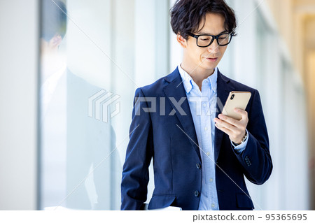 Smiling young man with smartphone in office corridor 95365695
