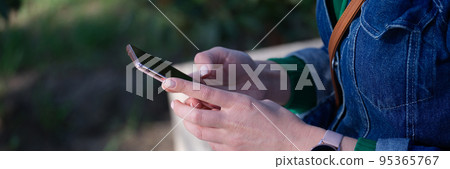Woman sitting on bench is holding smartphone 95365767