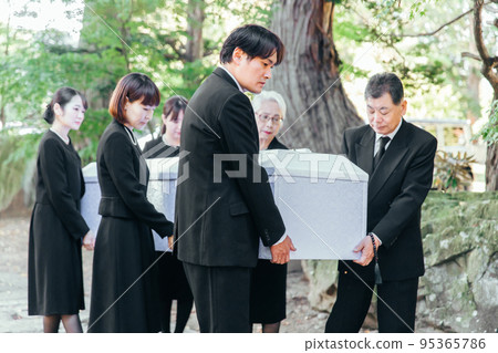 Bereaved family carrying coffin to hearse at funeral 95365786