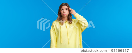 Gosh just kill me. Bored and pressured, stressed young blonde girl in yellow hoodie, make pistol gesture near head, shooting from gun and sighing as feel bothered and troubled, blue background 95366157