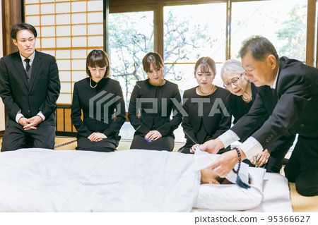 A bereaved family mourning the deceased around a futon at a funeral / wake A bereaved family mourning the deceased around a futon at a funeral / wake 95366627
