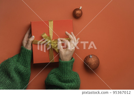 Female hands open Christmas red gift box with golden bow on the red background. Green sweater. New Year concept. Winter holidays and presents. Surprise delivery. Unpacking. Female hands open Christmas red gift box with golden bow on the red background. Green sweater. New Year concept. Winter holidays and presents. Surprise delivery. Unpacking. 95367012