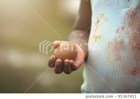 African-American child holding chicken egg with color stain on hand and dress. African-American child holding chicken egg with color stain on hand and dress. 95367451