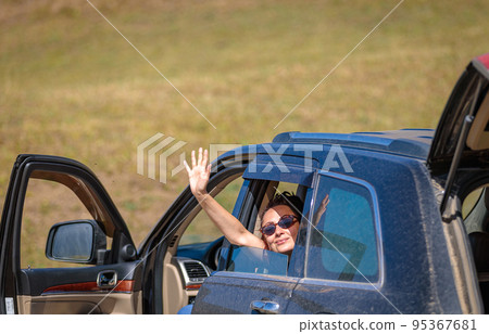 Smiling happy girl waving from the car window while traveling in the mountains. Smiling happy girl waving from the car window while traveling in the mountains. 95367681