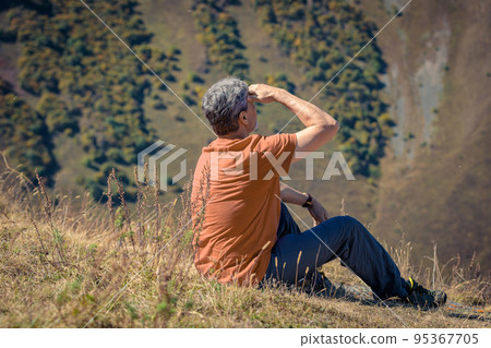 A man sits on top of a mountain and enjoys the scenery of the Caucasus Mountains. 95367705